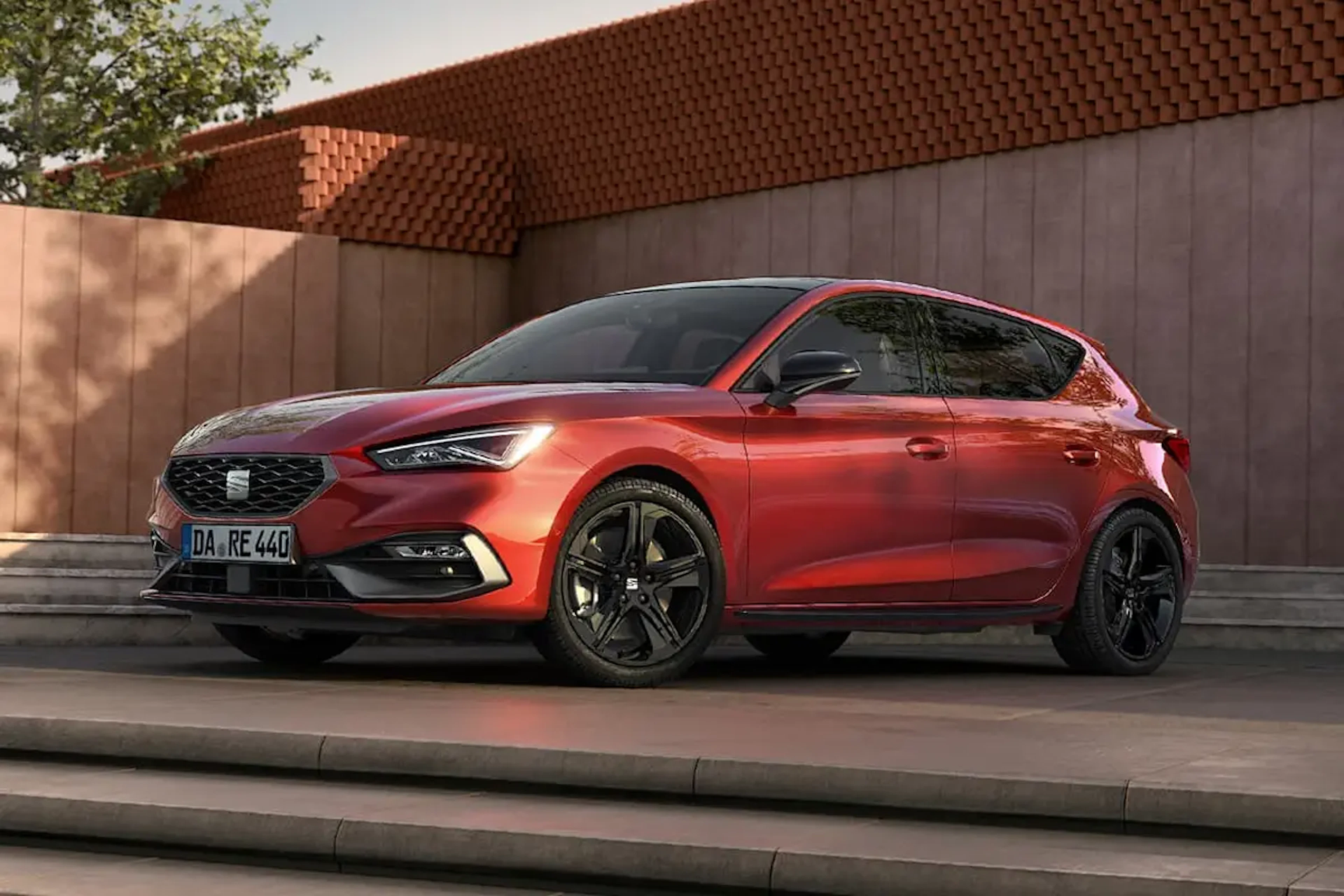 SEAT Leon FR Black Edition in Rot seitlich von vorne fotografiert, geparkt auf Stufen vor moderner Fassade